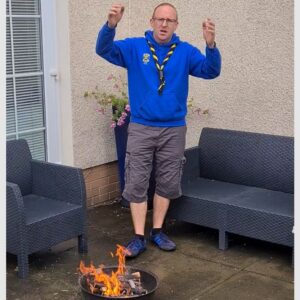 A photo of the camp chief singing campfire songs around a small fire pit in his back garden