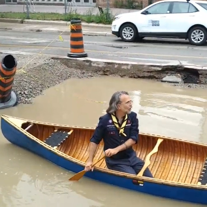 A photo of a canadian scout leader canoeing in a large puddle at the side of the road