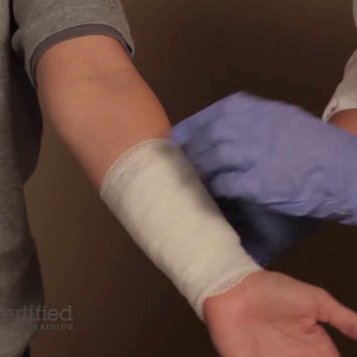 A photo of someone wearing gloves wrapping a bandage around someone's arm